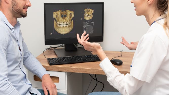 Dentista explicando a un paciente los resultados de una tomografía dental en una computadora, mostrando imágenes 3D de la estructura ósea y dentadura